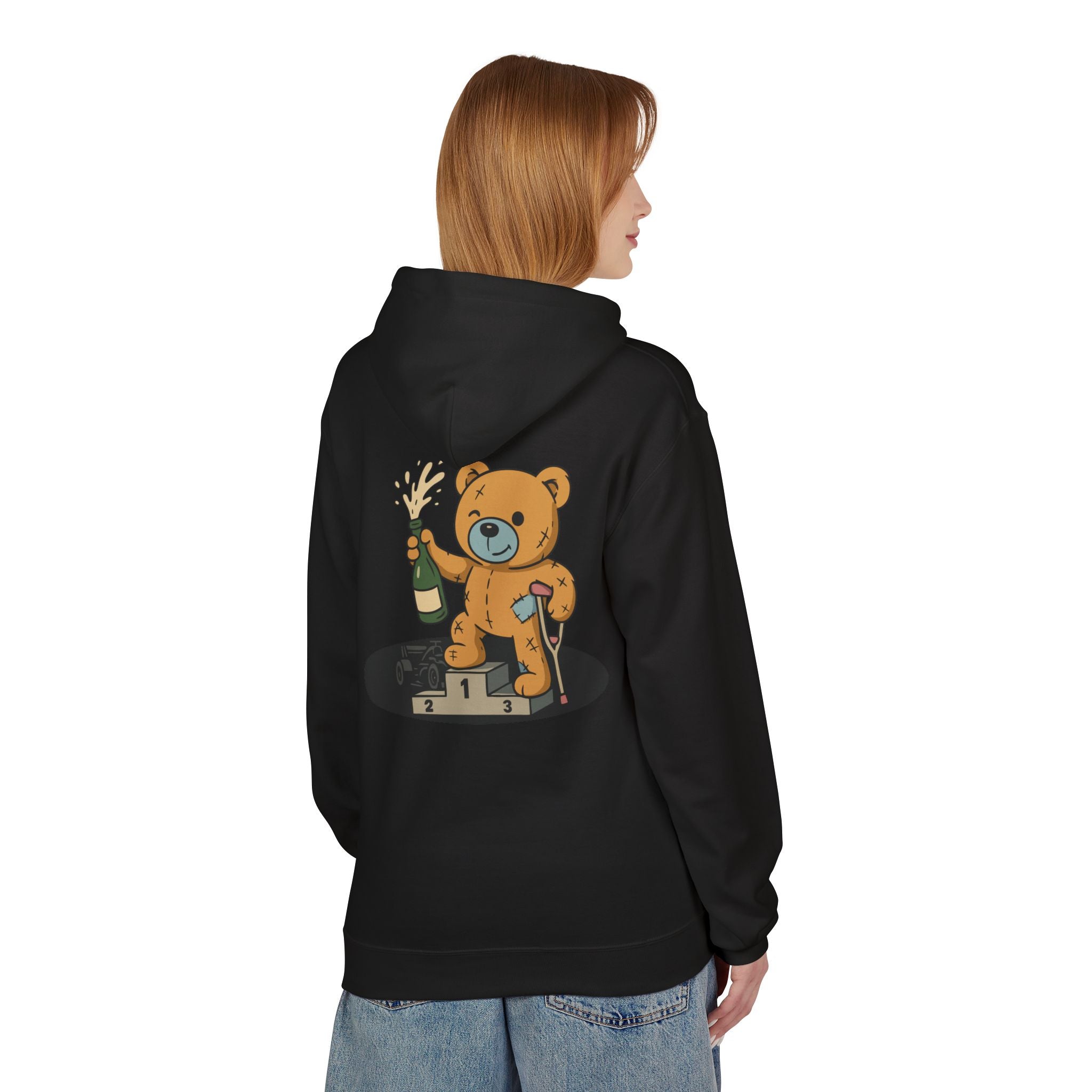 A person wears the Podium Bear Hoodie by Printify, featuring a cartoon teddy bear with a champagne bottle on a winners' podium. Eco-friendly crafted, this black hoodie combines style with sustainability.