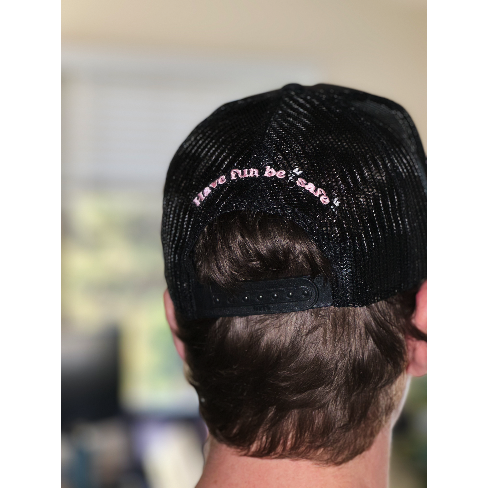 Rear view of a person wearing a Better not Classic Trucker (mid crown) with the phrase "have fun be safe" in pink.