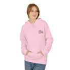 A person wearing an ethically made pink "The Script Hoodie" from Printify stands with hands in pockets against a plain white background.