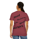 A person with braided hair wears a maroon Printify "Bad decisions" Tee made of 100% ring-spun cotton. Its garment-dyed fabric has the playful phrase "Bad decisions make good stories" on the back, adding whimsy and comfort to their style.