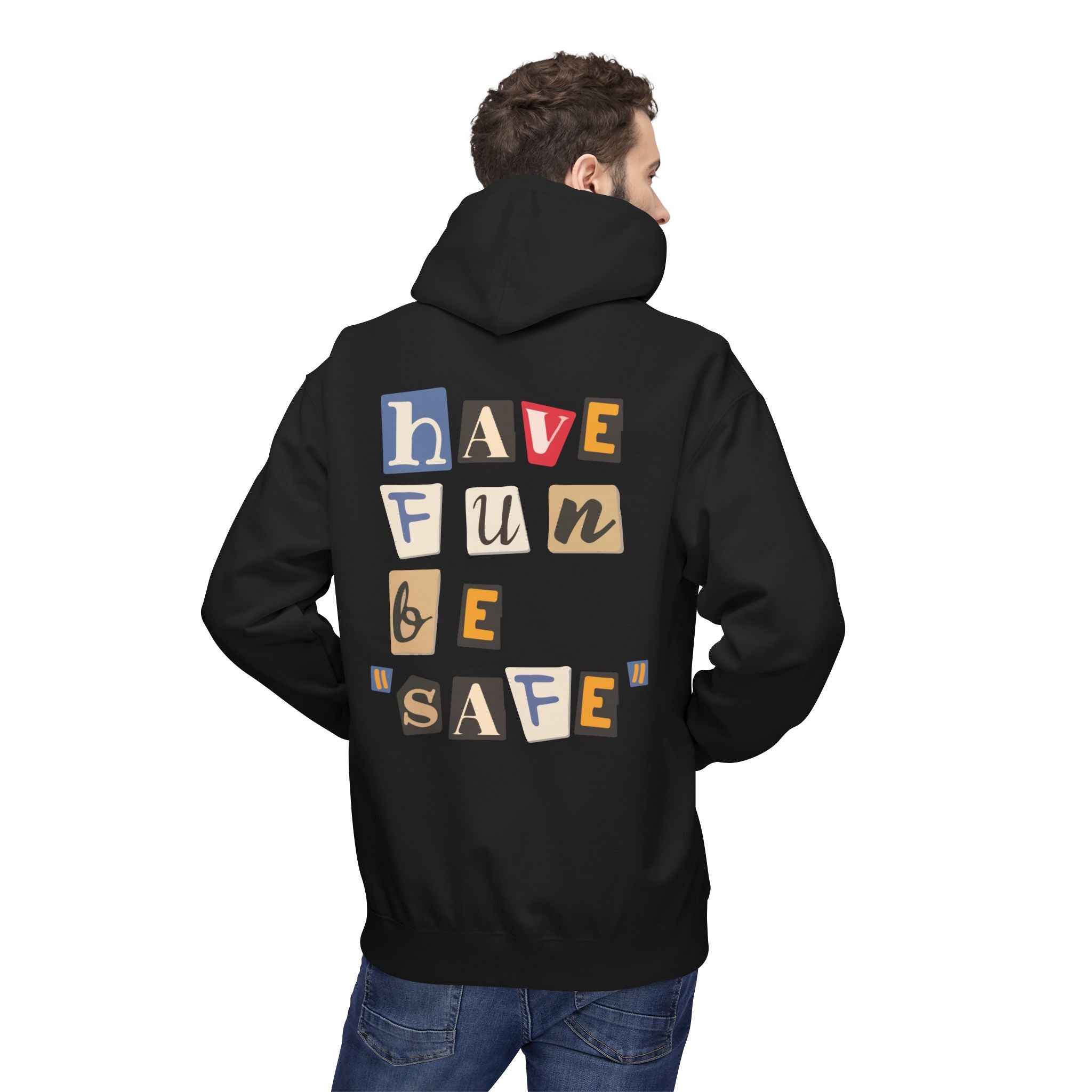 A man stands with hands in pockets facing away, wearing the eco-friendly Have Fun Be "Safe" Hoodie v3 from Printify. It's black, featuring colorful letters spelling out "have fun be safe" on the back.