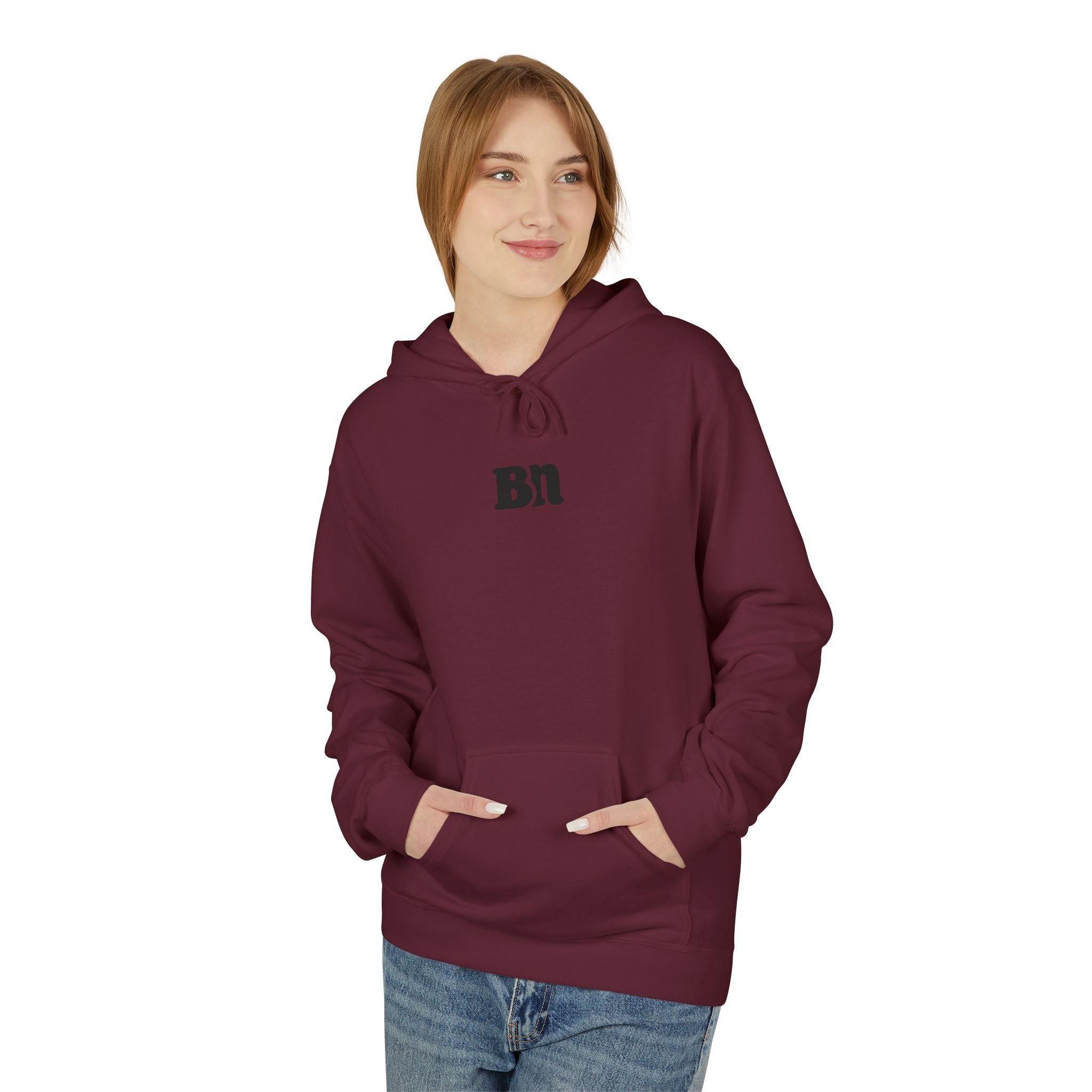 A person stands against a white background, wearing blue jeans and a maroon Bad Decisions Hoodie by Printify featuring "Bn" text, crafted in an eco-friendly facility, with hands in pockets.