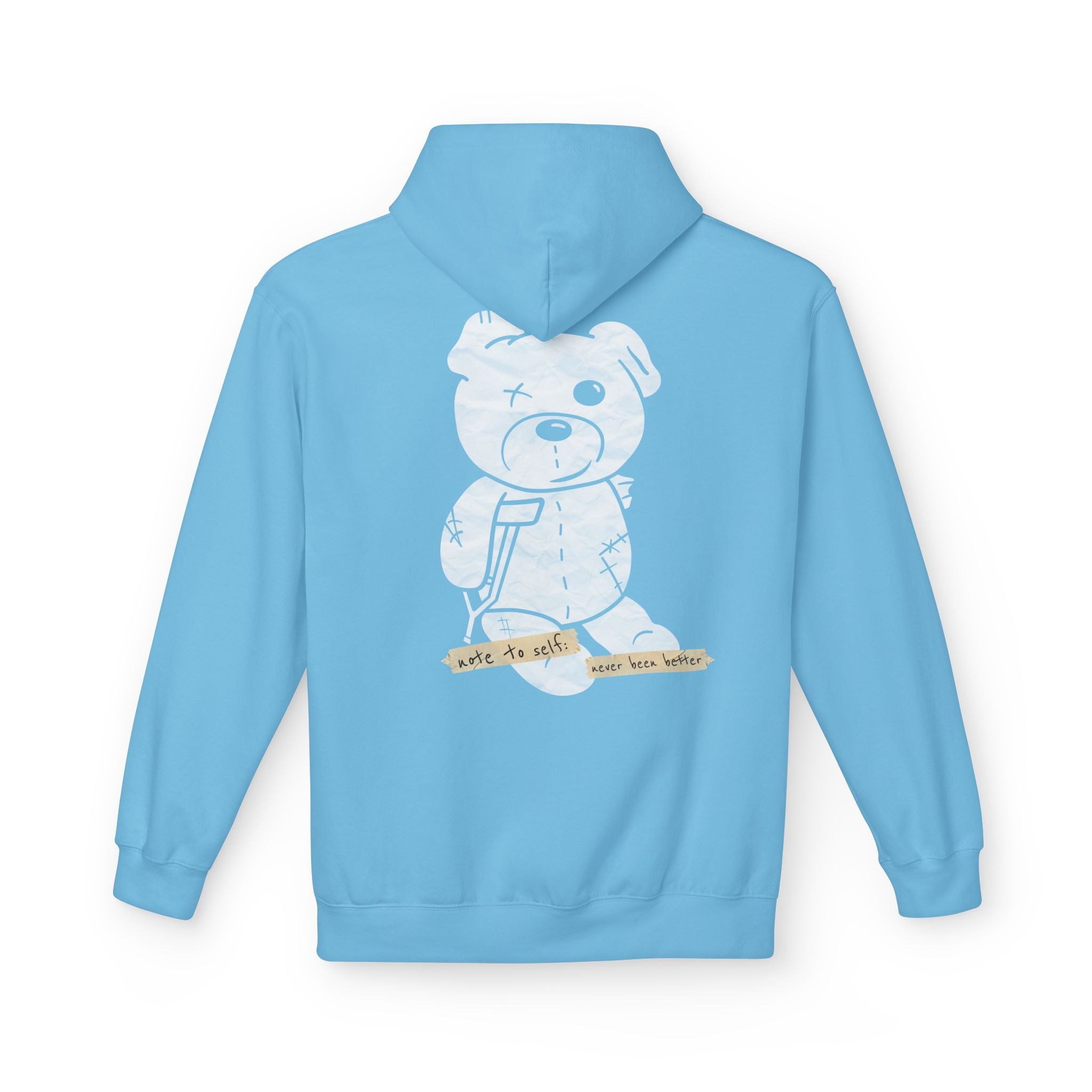 The "Note to self" Hoodie by Printify is a light blue hoodie featuring a white graphic of a bandaged teddy bear with crutches and the text "note to self: see the better." Made from eco-friendly materials, it combines sustainability with style.