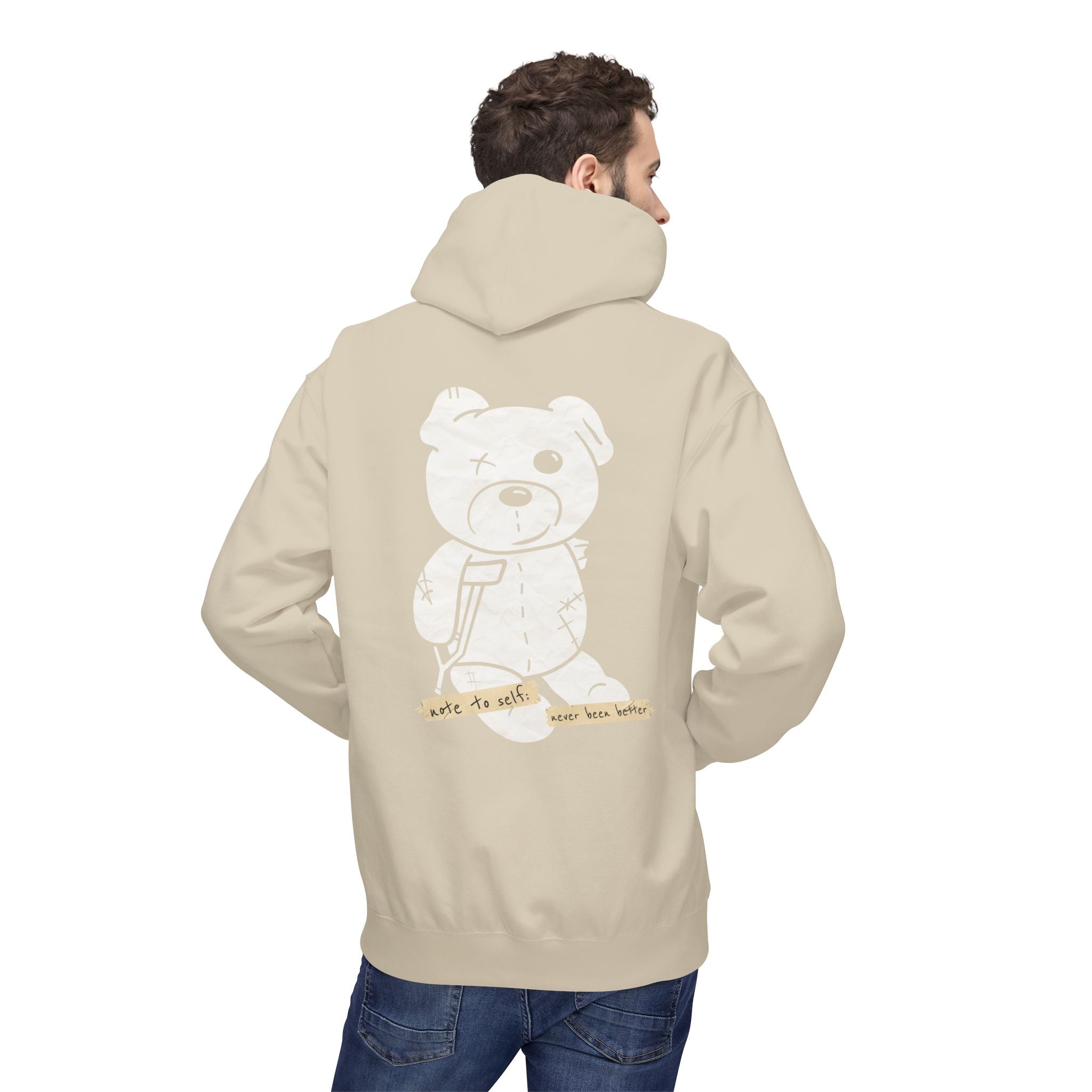 A person wearing a Printify "Note to self Hoodie" in sustainable beige, featuring a cartoon bear graphic on the back, paired with blue jeans.