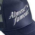 A close-up of the Almost Famous Trucker cap by Better not, featuring white "Almost Famous" embroidery on its dark blue front. This High-Crown Fit cap includes a mesh back and snapback closure.