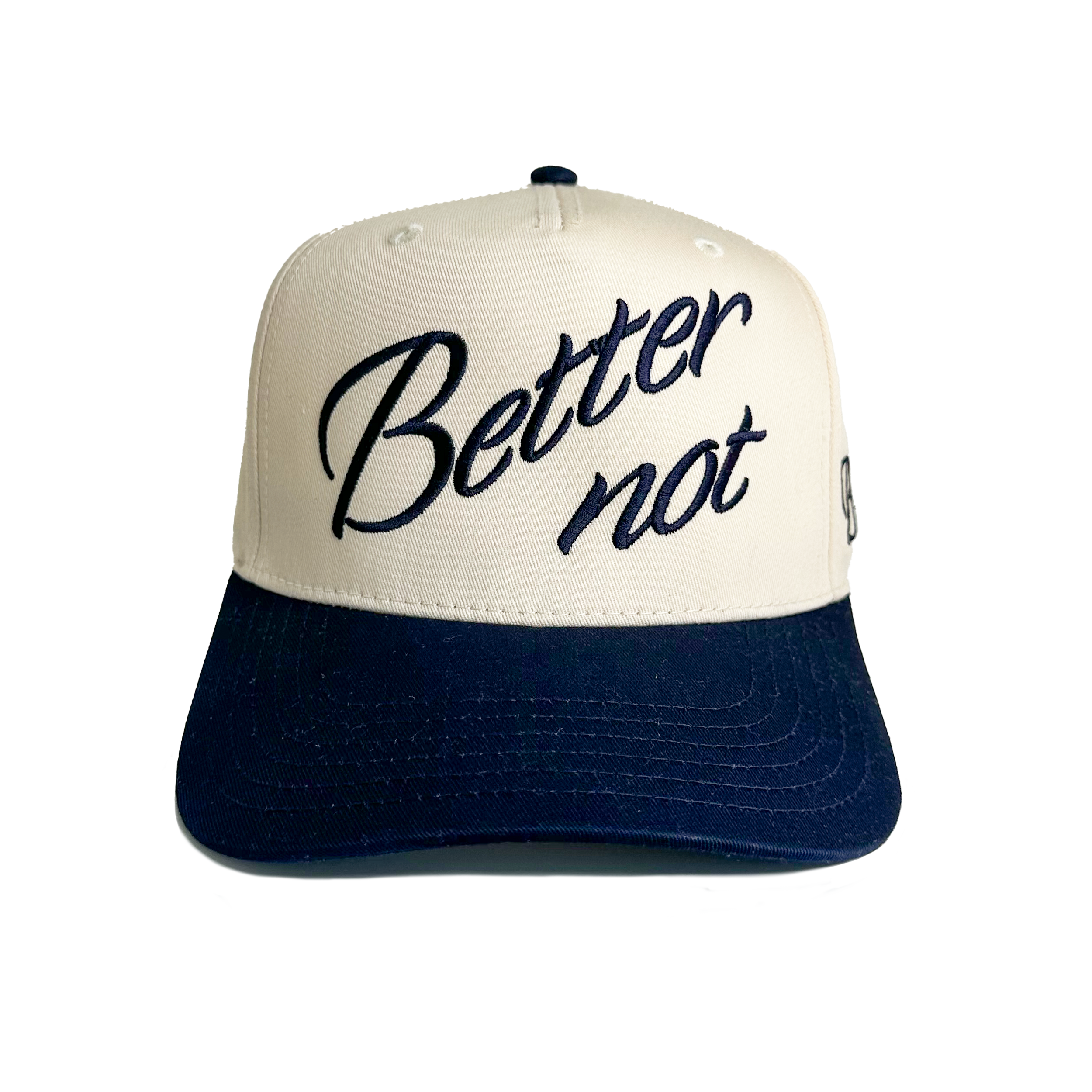 The Classic by Better not is a light cream cap with a white crown and a dark blue bill that features 3D embroidered artwork. The text on the front reads "Better not" in cursive font, adding a touch of flair. Its snapback closure ensures a comfortable fit for all.