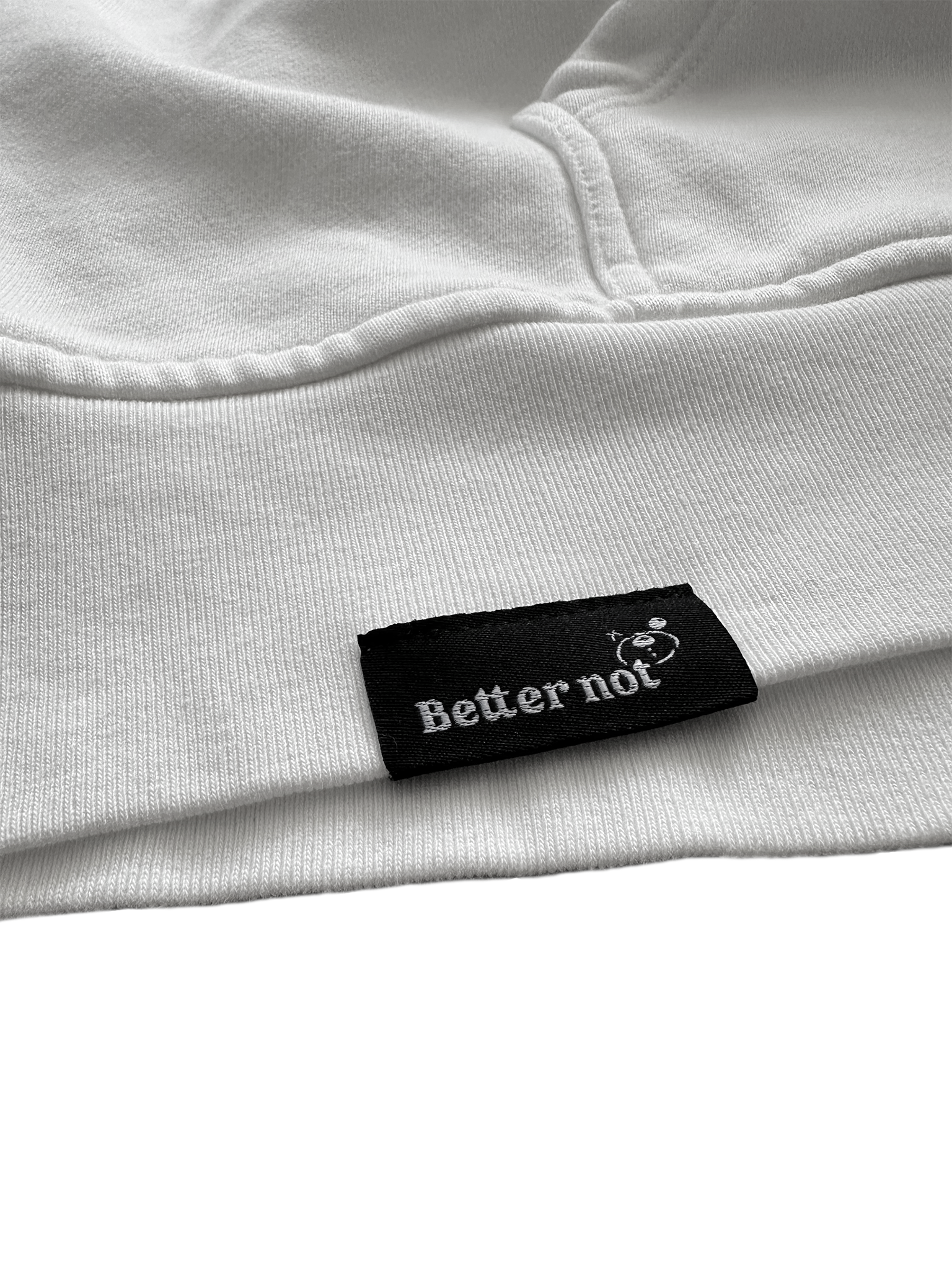 Close-up of the white Have Fun Be "Safe" Hoodie v2, crafted from brushed fleece, with a black label that has "Better not" and a small graphic symbol on it.