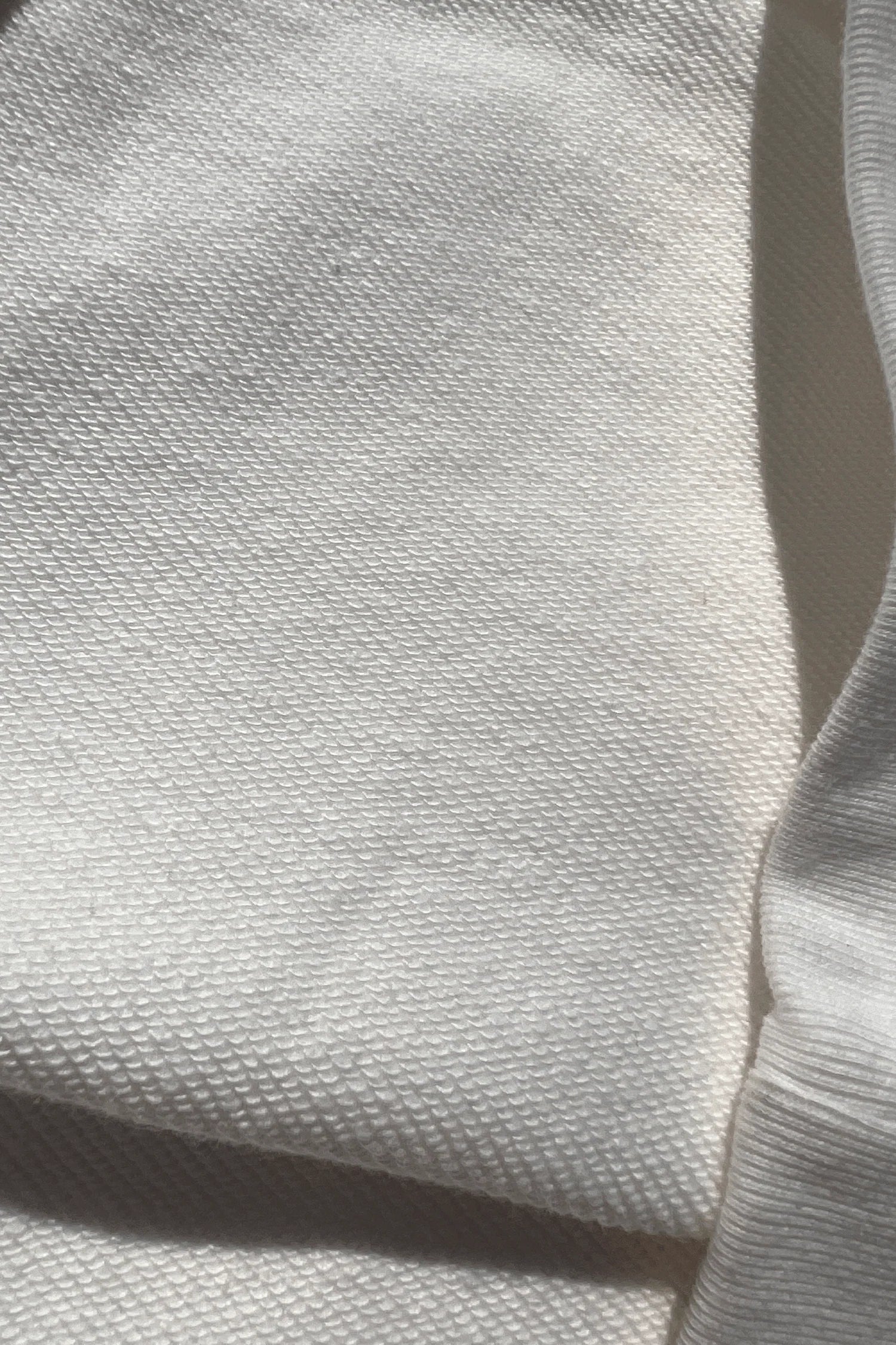 Close-up of a textured Better not organic cotton fabric with shadows and sunlight creating a pattern.