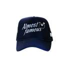 A premium navy blue Almost Famous Trucker baseball cap by Better not with the phrase "almost famous" embroidered in white, accompanied by a small graphic of a smiling face with sunglasses.